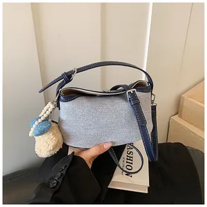 Dettaglio di una borsa a secchiello in denim azzurro con finiture blu navy e ciondolo in peluche