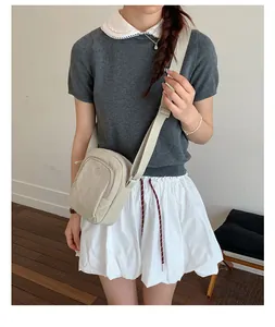 Modell trägt eine kleine beige Umhängetasche aus Nylon in einem lässigen Innenraum