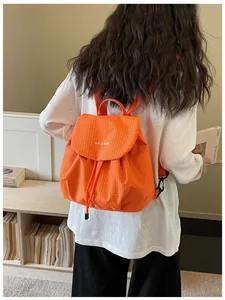 Detailed back view of a trendy orange plaid mini backpack worn by a female model.