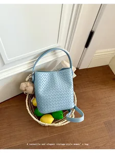 Detailed view of a light blue woven bucket bag with an elegant bear charm accessory