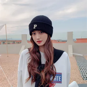 Woman wearing a black knitted beanie with a white 'P' embroidery in an outdoor setting