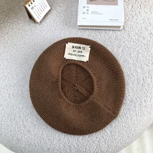 Detail view of brown knitted wool beret featuring a stylish letter patch decoration