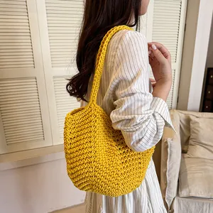 Close-up of a vibrant yellow handmade crochet shoulder bag carried by a female model in a room