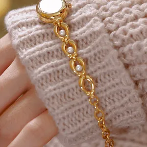 Dettaglio di un orologio vintage da donna dorato con bracciale di perle su manica