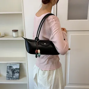Sac sous l'aisselle noir minimaliste avec breloque colorée porté par un mannequin