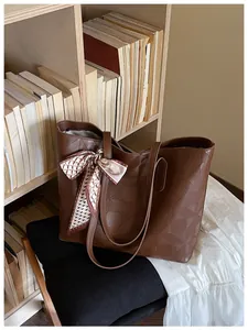 Brown geometric embossed tote bag with decorative scarf detail on a bookshelf context.