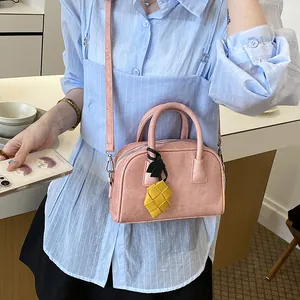 Stylish pink suede-like pillow bag with yellow woven pineapple charm worn by a model