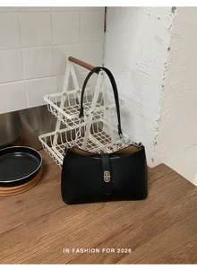 Primo piano di una borsa sottobraccio nera con fibbia argentata su un tavolo di legno.