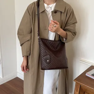 Elegant model met een donkerbruine retro geweven emmertas met grote capaciteit voor dagelijks gebruik