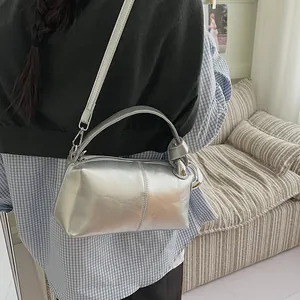 Detail of a silver metallic pillow bag with a knot handle shown on a model's shoulder.