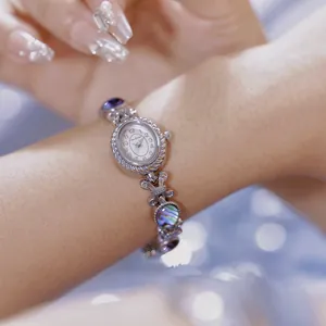Primer plano de reloj plateado para mujer con pulsera de concha de abulón iridiscente.