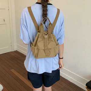 Vista trasera detallada de una mochila caqui con cordón llevada por una modelo en una sala