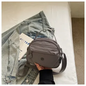 Primer plano del bolso bandolera gris de nailon con textura de tela y etiqueta de marca.