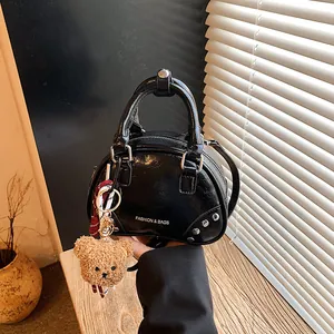 Detail view of black bowling bag with rivets and plush bear charm.
