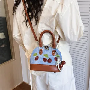 Minibolso bandolera de mezclilla azul con bordado de cerezas en modelo con traje blanco
