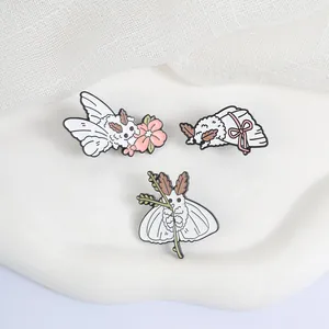 Gros plan sur trois adorables broches en émail de mites blanches avec fleurs et rubans.