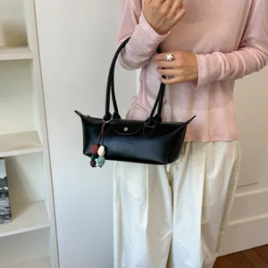 Sac sous le bras noir de niche tenu par un modèle dans un haut décontracté rose