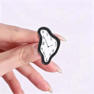 Detalle de un broche de esmalte de reloj derretido inspirado en Salvador Dalí entre dedos