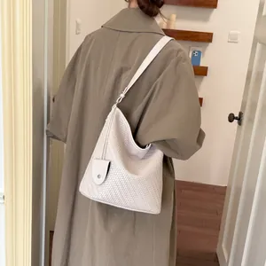Vrouw in kaki trenchcoat met een wit geweven hobo schoudertas met textuur.