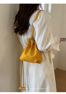 Yellow candy-colored minimalist drawstring bag worn by a model in a white dress.