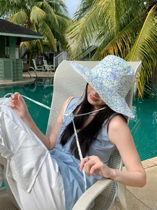 Model wearing a blue floral lace bucket hat by a tropical pool for summer sun protection.