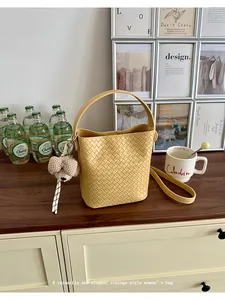 Close-up of a vintage-style yellow woven bucket bag with a teddy bear charm on a table