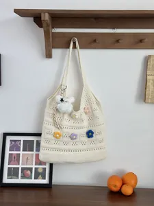 Handgefertigte Häkel-Tragetasche mit bunten Blumenakzenten und Plüsch-Anhänger.