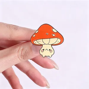Detailed view of a cute anthropomorphic orange mushroom enamel pin held for size reference