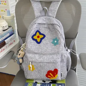 Detailed view of a grey student backpack with cute plush flower patches and bear charm