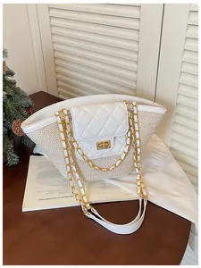 Détail du rabat blanc matelassé et chaîne dorée sur le sac panier d'été en paille