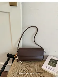 Brown minimalist baguette shoulder bag with beaded charm presented on a stylish woven chair