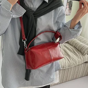 Detailed close-up showing the glossy texture of a retro red pillow bag worn as a crossbody