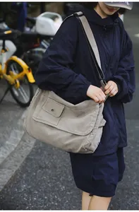 Casual large capacity gray canvas messenger bag shown on model in an outdoor city setting