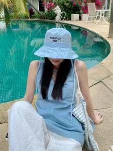 Modella asiatica con un cappello alla pescatora a quadretti azzurro a bordo piscina