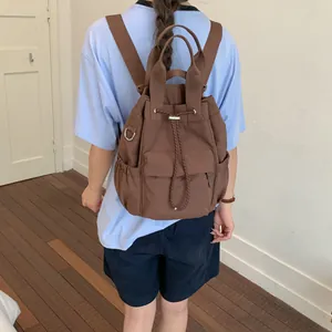 Vista trasera de una mochila marrón con cordón en una modelo con una camiseta azul claro