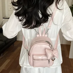 Rückansicht eines modischen rosa Mini-Rucksacks mit dekorativem Schleifenanhänger an einer Frau