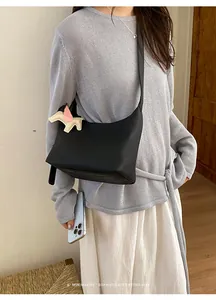 Detailed view of chic minimalist slouchy black shoulder bag with cute winged horse charm.