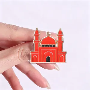 Primer plano de un pin de mezquita de esmalte rojo con media luna sostenido por los dedos