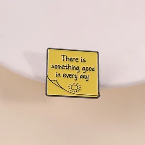 Detalle de un pin esmaltado amarillo con una frase motivadora en inglés muy positivo