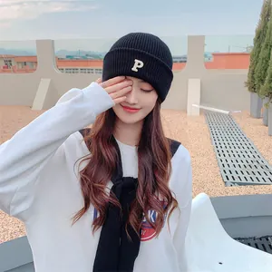 Stylish black knitted beanie with 'P' letter embroidery worn by model on rooftop