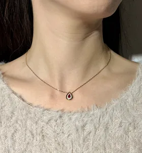 Close-up of elegant gold teardrop necklace with red stone pendant worn by model.