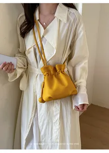Stylish yellow drawstring crossbody bag paired with a beige trench coat for a retro vibe.