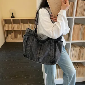 Détail d'un grand sac cabas en denim délavé porté par un mannequin en bibliothèque