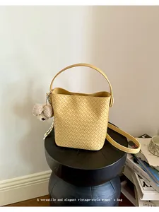 Detailed view of a yellow woven bucket bag with a bear charm on a vintage stool