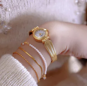 Primer plano de un elegante reloj dorado con correa de espiga y pulseras de perlas