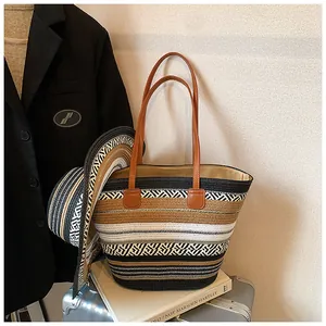 Gestreifte Strohtasche mit großem Fassungsvermögen und passendem Sonnenhut auf Koffer.