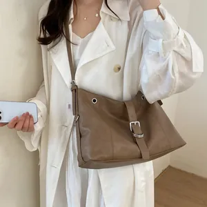 Model carrying a stylish brown leather hobo shoulder bag with a silver buckle strap.