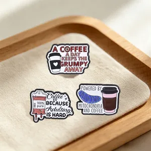 Close-up detail of funny coffee-themed enamel pins displayed on a wooden tray with soft fabric