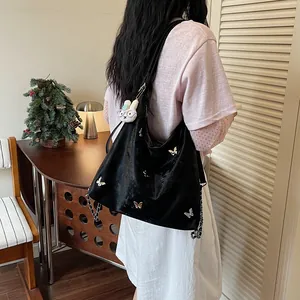 Detailed view of a black tote bag featuring silver butterfly studs and a plush rabbit charm
