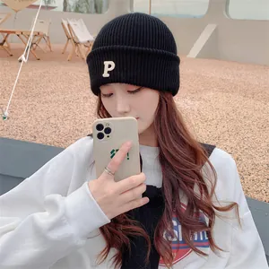 Stylish Asian woman wearing a black ribbed knit beanie with embroidered letter P